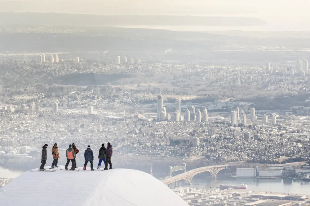 Anthill cinematographer, Matt Butterworth prepping for a shot with Red Bull unCorked athletes and Vancouver skyline in the distance. Photo Jussi Grznar. Grouse Mountain, North Vancouver ski resort, city skyline in winter, Vancouver snow,